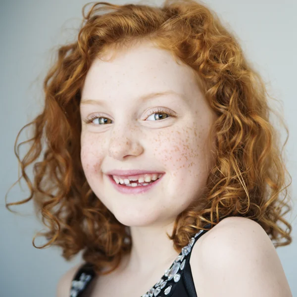 young girl with red hair and freckles smiling with new teeth growing in
