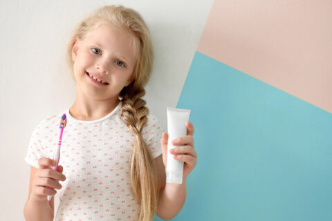 A girl showing tooth brush and toothpaste in her hands while smiling