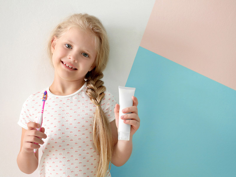 A girl showing tooth brush and toothpaste in her hands while smiling